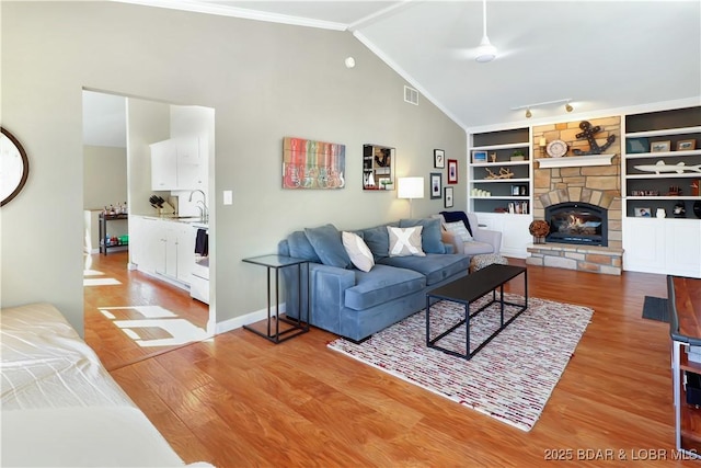 living room featuring built in features, visible vents, ornamental molding, a stone fireplace, and light wood-type flooring