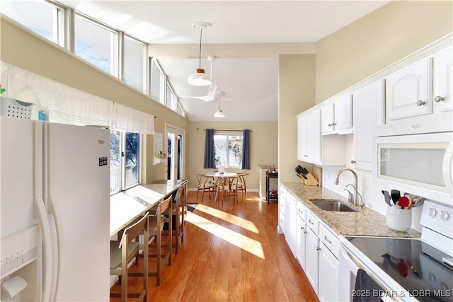 kitchen featuring light stone counters, light wood finished floors, white cabinets, a sink, and white appliances