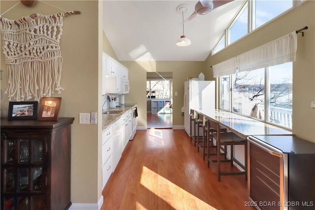 kitchen featuring white appliances, a sink, white cabinets, light wood finished floors, and plenty of natural light