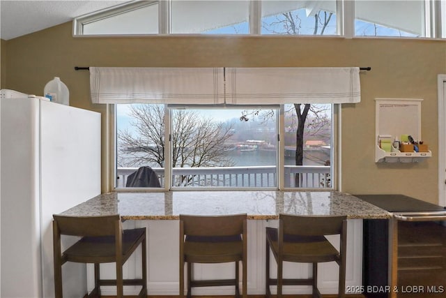 kitchen with vaulted ceiling, breakfast area, freestanding refrigerator, and light stone countertops