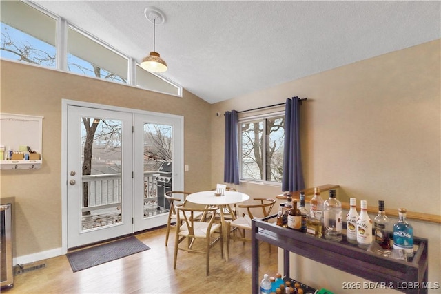 dining space featuring a textured ceiling, beverage cooler, wood finished floors, baseboards, and vaulted ceiling