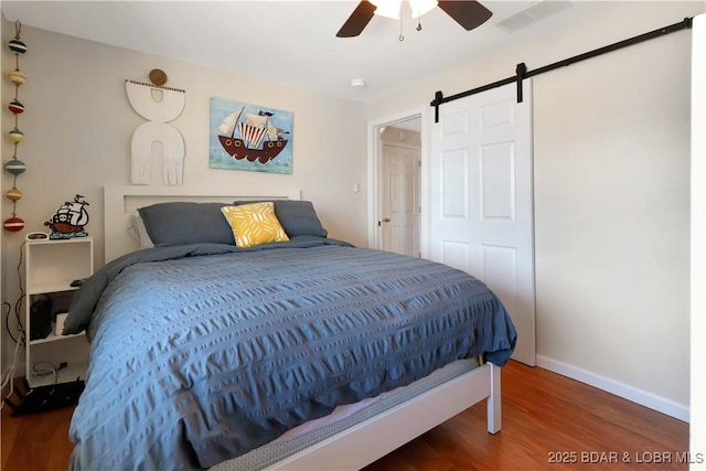 bedroom with a barn door, visible vents, baseboards, ceiling fan, and wood finished floors