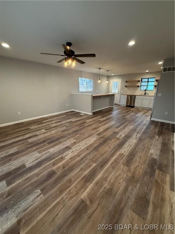 unfurnished living room with ceiling fan, plenty of natural light, dark wood finished floors, and baseboards