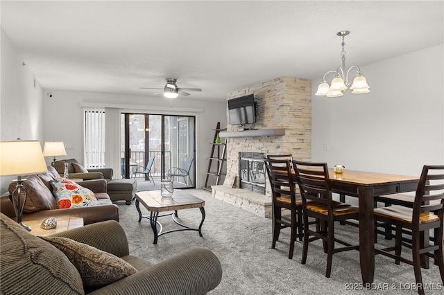 living room featuring ceiling fan with notable chandelier, carpet floors, and a stone fireplace