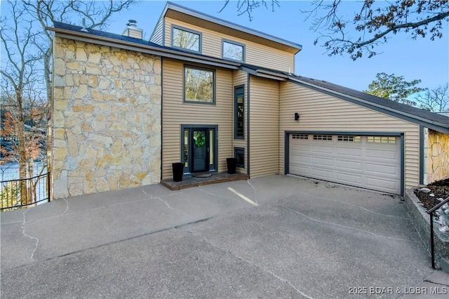 view of front of property with stone siding, driveway, a chimney, and an attached garage