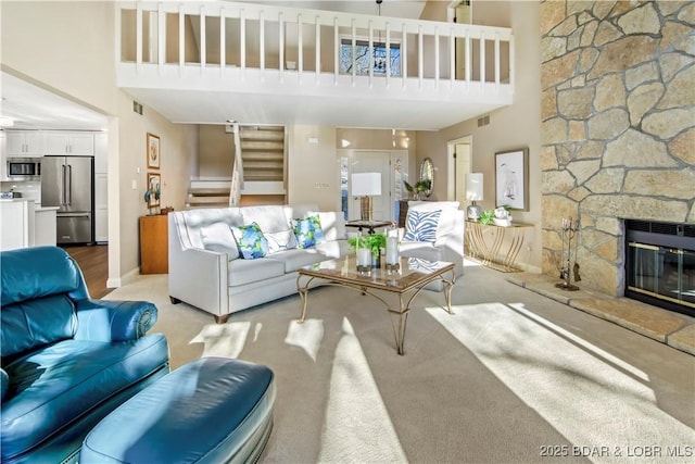 living area featuring a towering ceiling, stairs, visible vents, and a stone fireplace