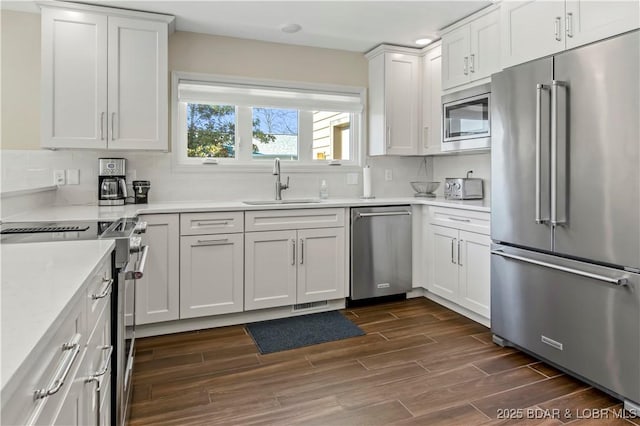 kitchen with stainless steel appliances, wood finish floors, a sink, white cabinets, and light countertops