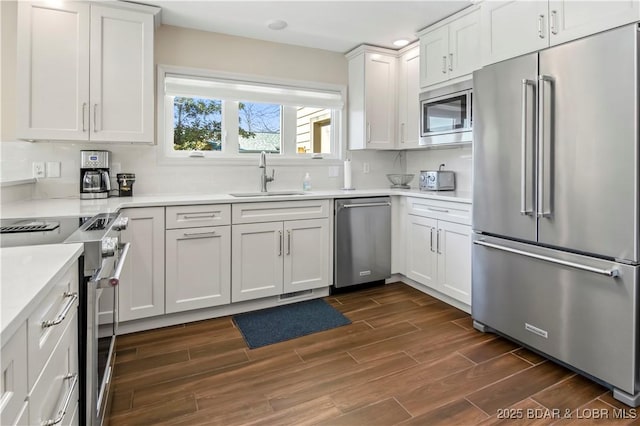 kitchen featuring light countertops, wood tiled floor, white cabinetry, a sink, and high quality appliances