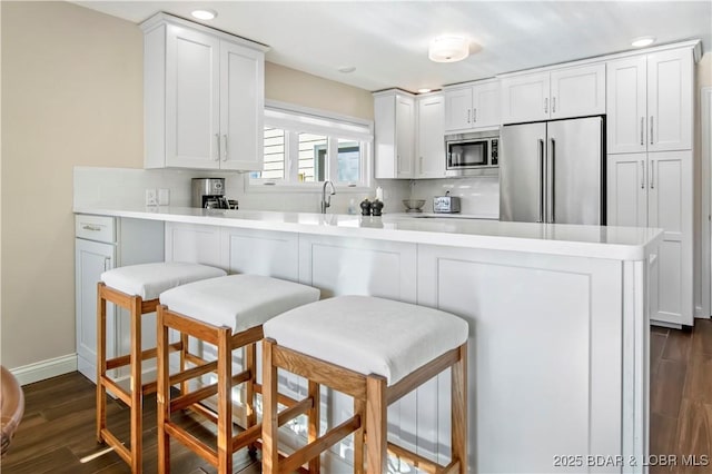 kitchen featuring a kitchen bar, dark wood-style flooring, stainless steel appliances, and decorative backsplash