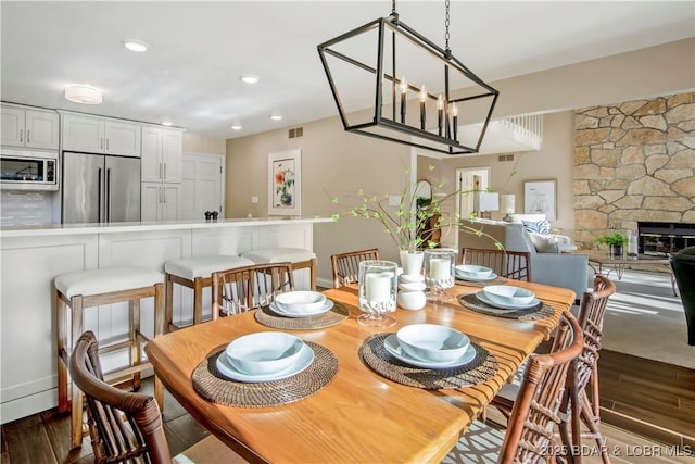 dining area featuring dark wood-type flooring, recessed lighting, visible vents, and a stone fireplace