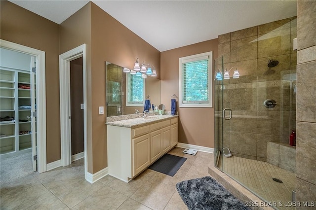 bathroom featuring vanity, baseboards, a shower stall, tile patterned floors, and a walk in closet