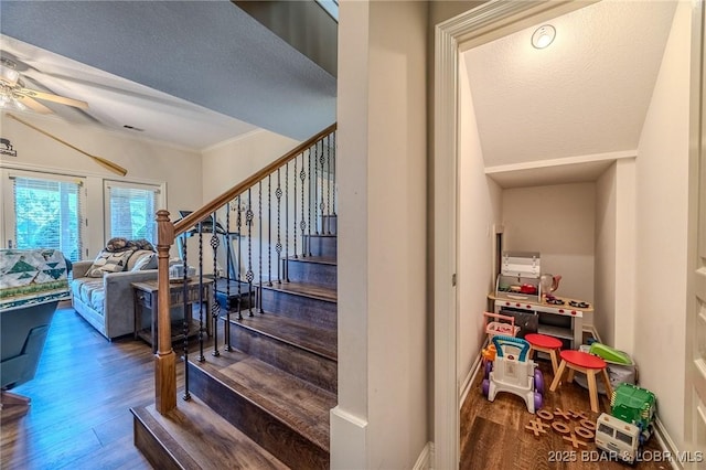 staircase featuring ceiling fan, a textured ceiling, wood finished floors, baseboards, and crown molding