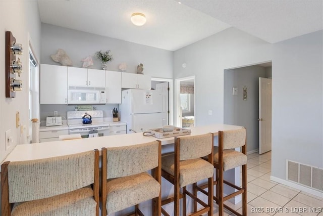kitchen with white appliances, a breakfast bar, light countertops, white cabinetry, and visible vents