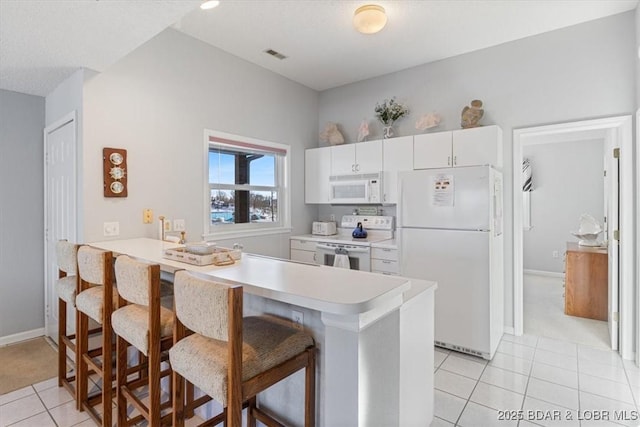 kitchen featuring a kitchen breakfast bar, light countertops, light tile patterned flooring, white appliances, and a peninsula