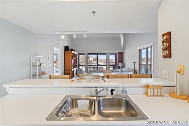 kitchen featuring rail lighting, open floor plan, a sink, and light countertops