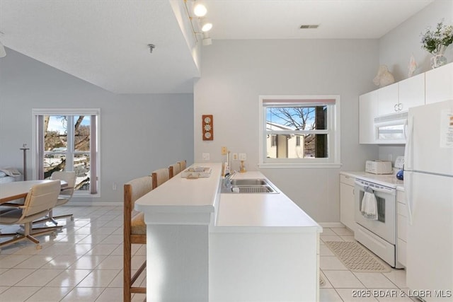 kitchen featuring white appliances, light tile patterned floors, a sink, a peninsula, and a kitchen breakfast bar