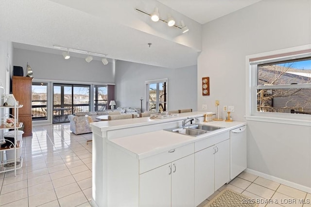 kitchen featuring a sink, light tile patterned floors, rail lighting, white dishwasher, and a peninsula