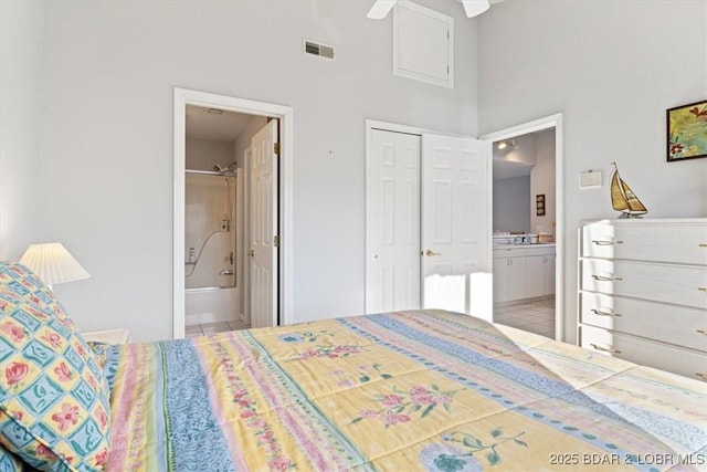 bedroom featuring ensuite bath, tile patterned flooring, a closet, visible vents, and a towering ceiling