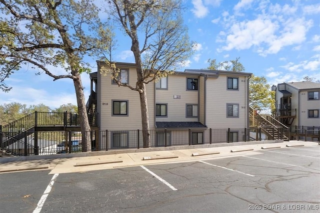 view of property featuring fence, uncovered parking, and stairs