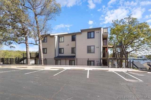 view of property featuring stairway, uncovered parking, and fence