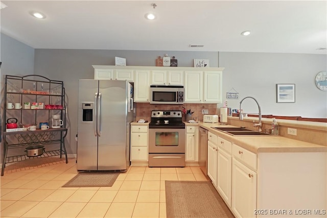 kitchen featuring light tile patterned floors, a peninsula, a sink, stainless steel appliances, and backsplash