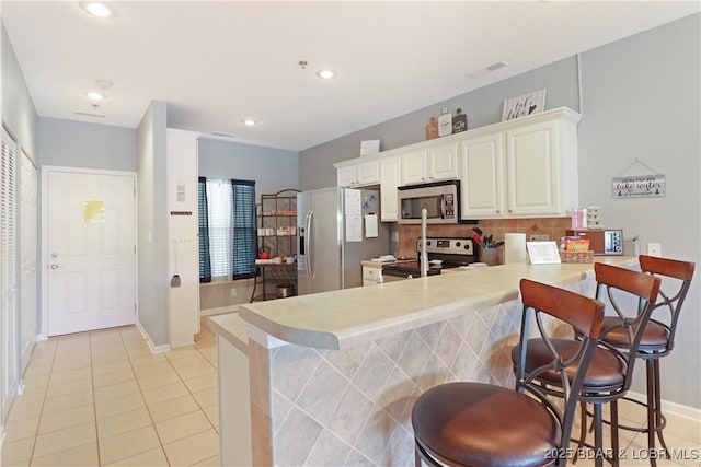 kitchen with a peninsula, appliances with stainless steel finishes, backsplash, and light countertops