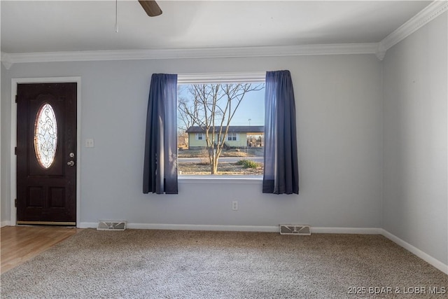 carpeted foyer featuring ornamental molding, a ceiling fan, visible vents, and baseboards