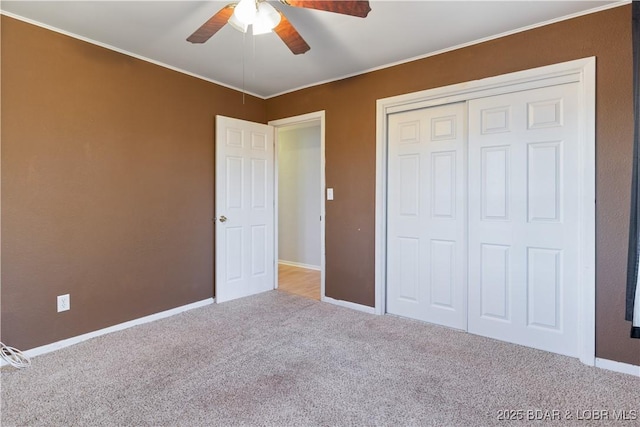 unfurnished bedroom with carpet floors, a ceiling fan, baseboards, ornamental molding, and a closet