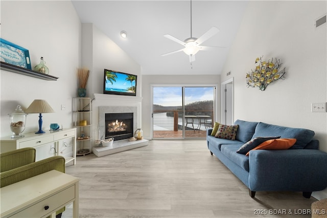 living area with high vaulted ceiling, visible vents, a high end fireplace, a ceiling fan, and light wood finished floors