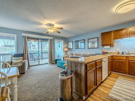 kitchen with dishwasher, brown cabinets, a peninsula, light countertops, and backsplash