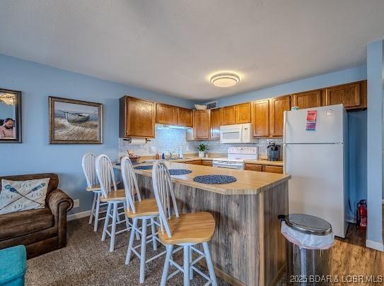 kitchen with white appliances, a breakfast bar, light countertops, backsplash, and brown cabinets