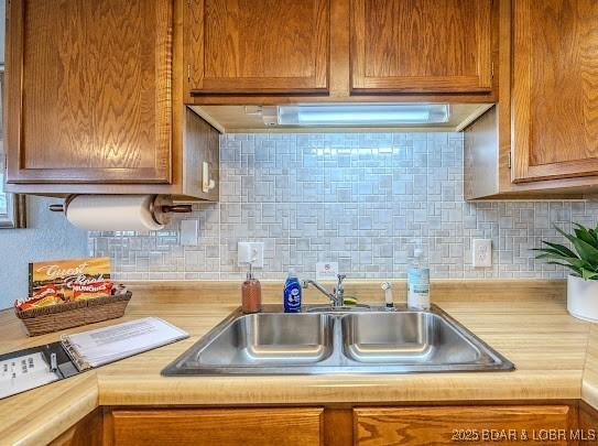 kitchen featuring tasteful backsplash, brown cabinetry, light countertops, and a sink