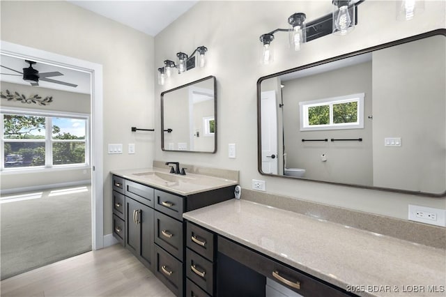 bathroom featuring toilet, wood finished floors, vanity, baseboards, and a ceiling fan