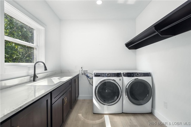 washroom with light wood-style flooring, a sink, baseboards, cabinet space, and washing machine and clothes dryer