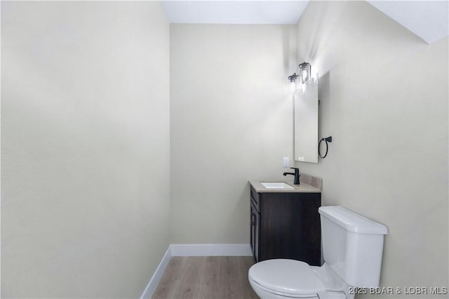 half bath featuring vanity, wood finished floors, toilet, and baseboards