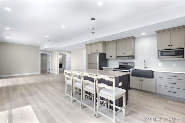 kitchen featuring stainless steel appliances, light countertops, gray cabinetry, a sink, and under cabinet range hood