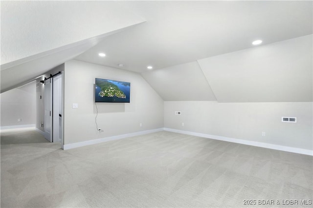 additional living space with lofted ceiling, recessed lighting, light colored carpet, a barn door, and baseboards