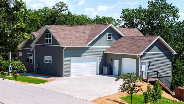 view of front facade with concrete driveway, roof with shingles, central AC, and an attached garage