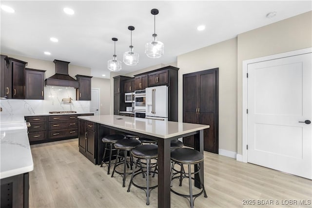 kitchen with light wood-style flooring, a kitchen island, custom exhaust hood, stainless steel gas stovetop, and high end fridge