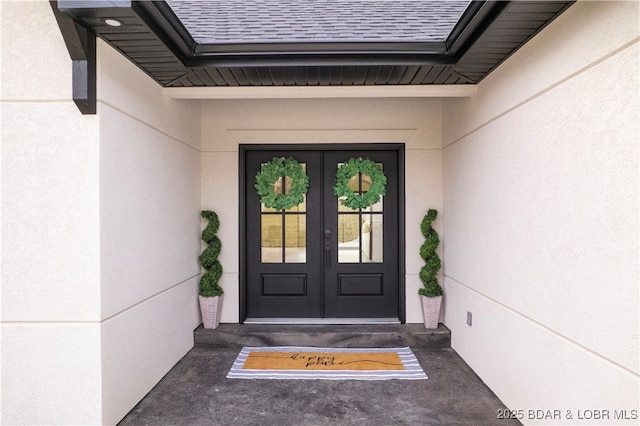 property entrance with stucco siding, french doors, and a shingled roof