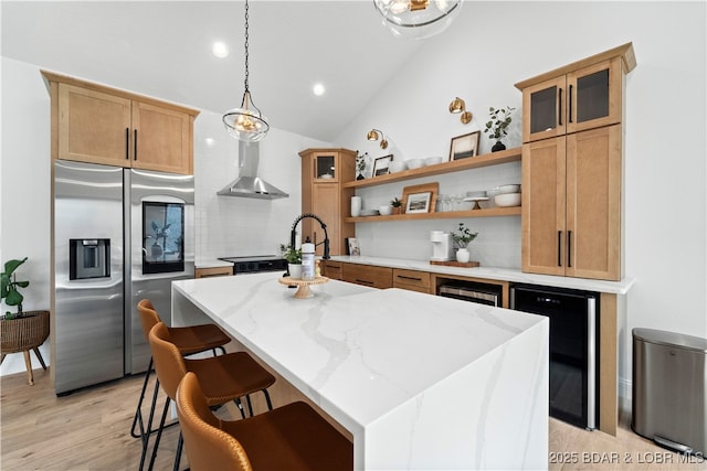 kitchen featuring beverage cooler, open shelves, an island with sink, wall chimney range hood, and stainless steel fridge