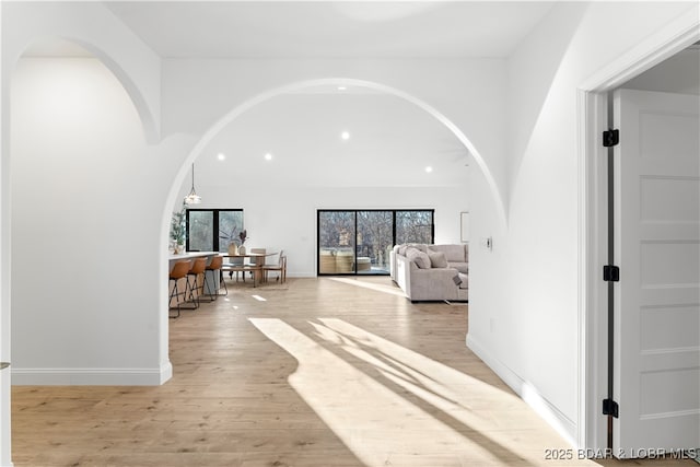 hallway with recessed lighting, baseboards, arched walkways, and light wood-style flooring