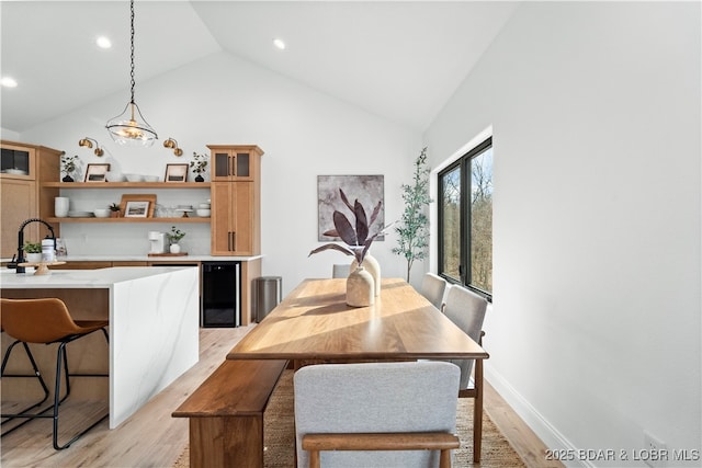 dining room with baseboards, wine cooler, light wood-style floors, and high vaulted ceiling