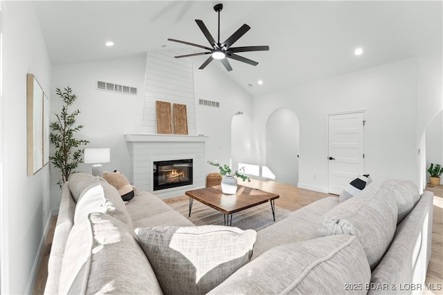 living room featuring arched walkways, visible vents, light wood finished floors, and a fireplace