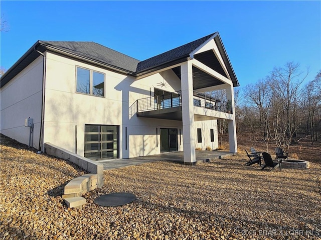 rear view of property with a fire pit, roof with shingles, an attached garage, a balcony, and ceiling fan