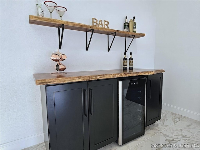 bar featuring a bar, beverage cooler, marble finish floor, and baseboards