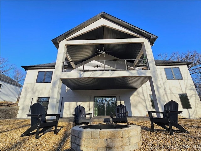 rear view of property featuring stucco siding, a balcony, a patio area, and an outdoor fire pit