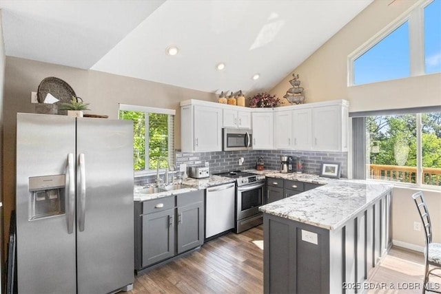 kitchen with appliances with stainless steel finishes, a peninsula, light stone countertops, a sink, and backsplash