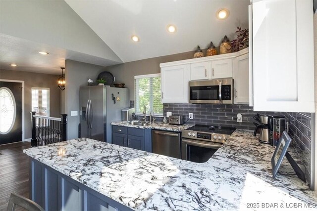 kitchen featuring appliances with stainless steel finishes, white cabinetry, vaulted ceiling, and light stone counters