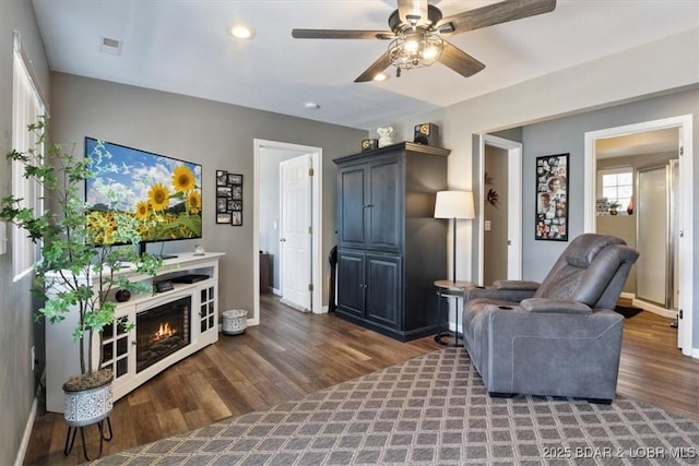 living area featuring visible vents, baseboards, a ceiling fan, wood finished floors, and a lit fireplace